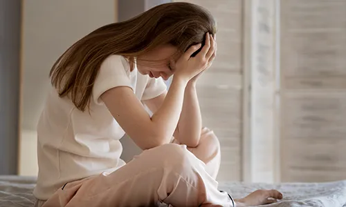 Mujer joven sentada con expresión de cansancio y agotamiento, sosteniendo su cabeza entre las manos.